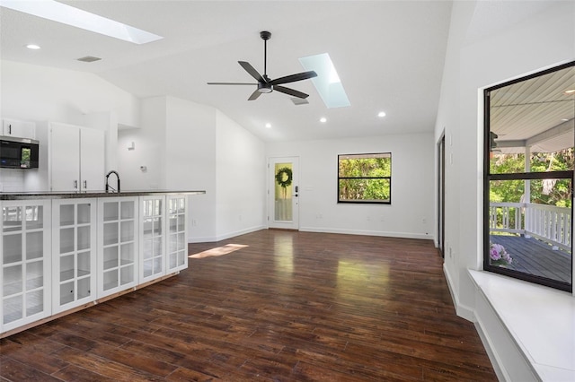 unfurnished living room featuring sink, dark hardwood / wood-style flooring, ceiling fan, and vaulted ceiling with skylight