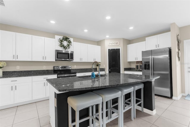 kitchen with white cabinetry, stainless steel appliances, sink, and a center island with sink