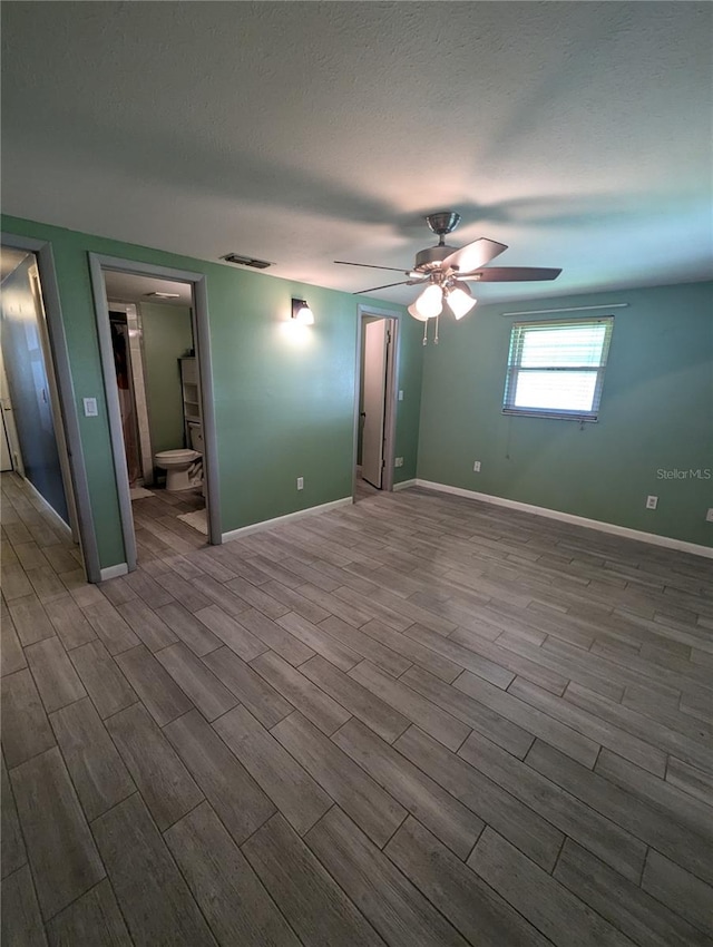 unfurnished bedroom with a textured ceiling, ensuite bathroom, wood-type flooring, and ceiling fan