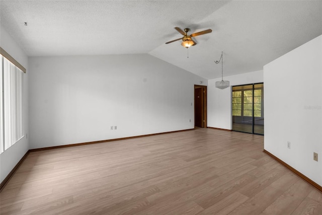 spare room featuring ceiling fan with notable chandelier, light wood-type flooring, and vaulted ceiling