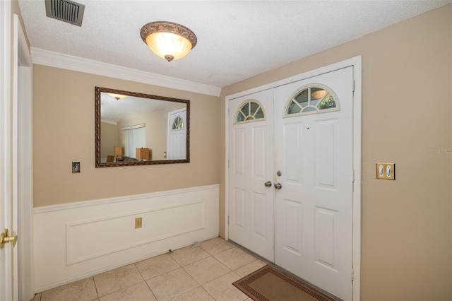 entryway with a textured ceiling, crown molding, and light tile patterned flooring