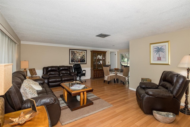 living room with light wood-type flooring, ornamental molding, and a textured ceiling