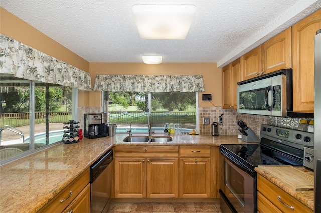 kitchen featuring backsplash, light stone countertops, stainless steel appliances, sink, and a textured ceiling