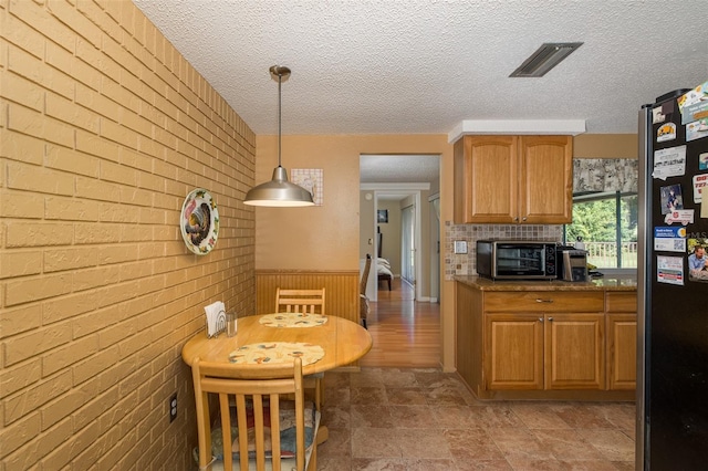 kitchen featuring a textured ceiling, brick wall, pendant lighting, and stainless steel fridge