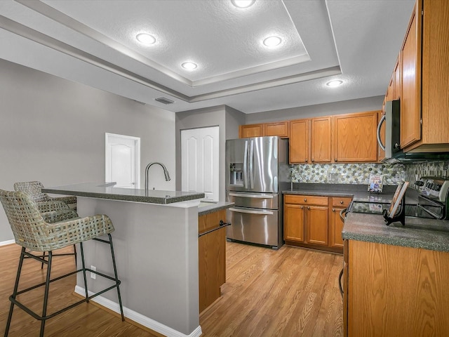 kitchen with a kitchen bar, a center island with sink, appliances with stainless steel finishes, light hardwood / wood-style flooring, and backsplash