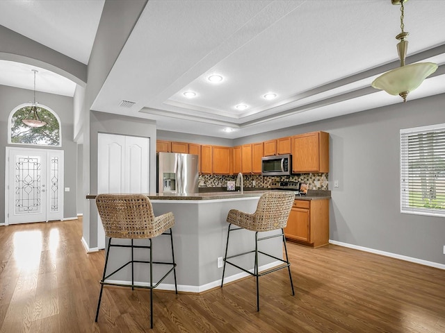 kitchen with light wood-type flooring, stainless steel appliances, backsplash, and a raised ceiling