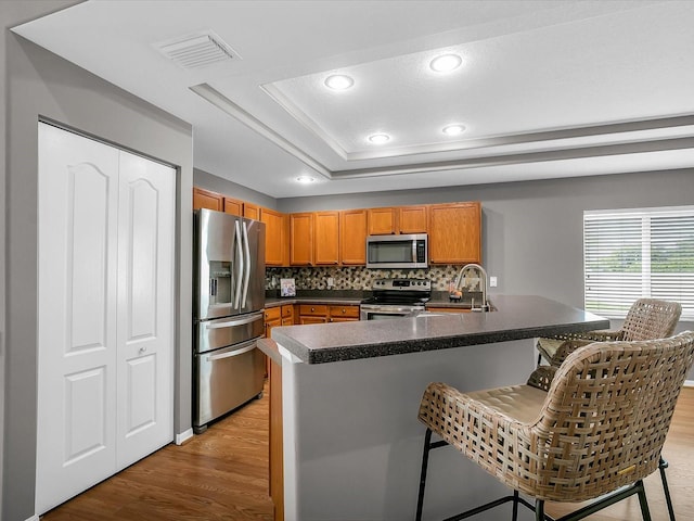 kitchen featuring a kitchen island with sink, stainless steel appliances, light hardwood / wood-style floors, decorative backsplash, and sink