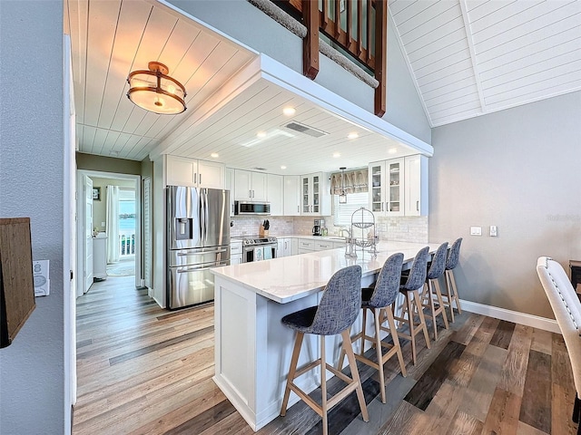 kitchen featuring stainless steel appliances, a kitchen breakfast bar, white cabinets, decorative backsplash, and kitchen peninsula