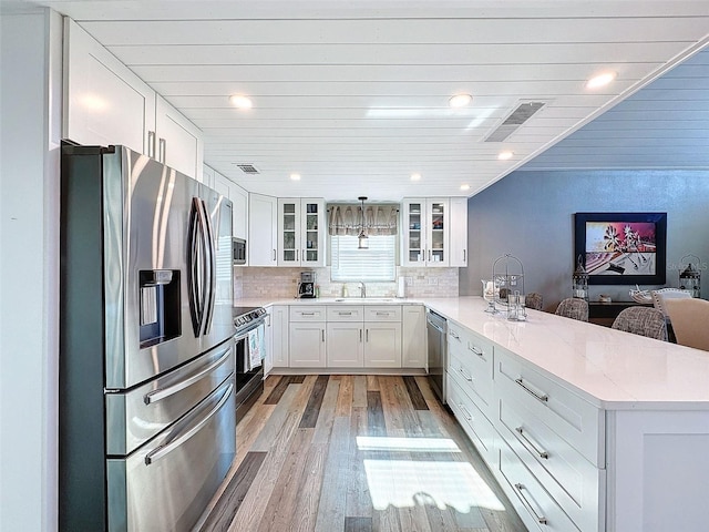 kitchen with sink, white cabinets, kitchen peninsula, stainless steel appliances, and light stone countertops