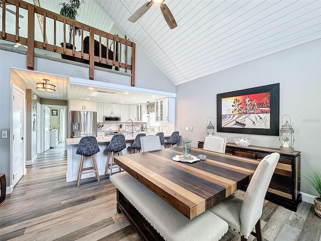 dining space with sink, high vaulted ceiling, ceiling fan, and light wood-type flooring