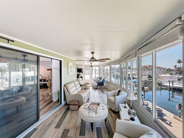 sunroom with plenty of natural light, ceiling fan, and a water view