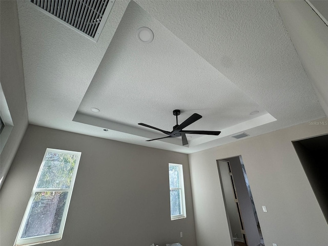 details with a tray ceiling, visible vents, and ceiling fan