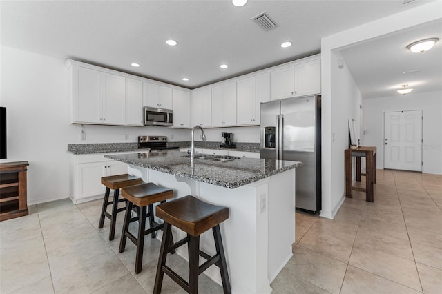 kitchen with sink, white cabinetry, dark stone countertops, stainless steel appliances, and a kitchen island with sink