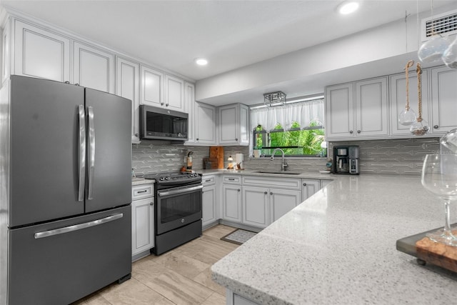 kitchen with light stone counters, sink, tasteful backsplash, and stainless steel appliances