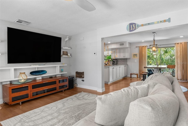 living room featuring ceiling fan, light hardwood / wood-style floors, and a textured ceiling