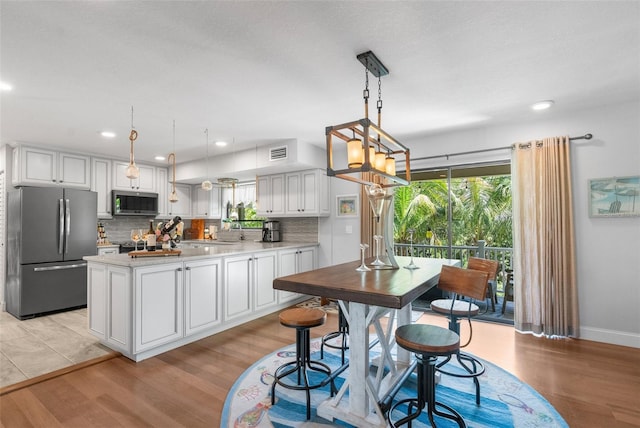 kitchen featuring appliances with stainless steel finishes, decorative backsplash, white cabinets, decorative light fixtures, and light wood-type flooring