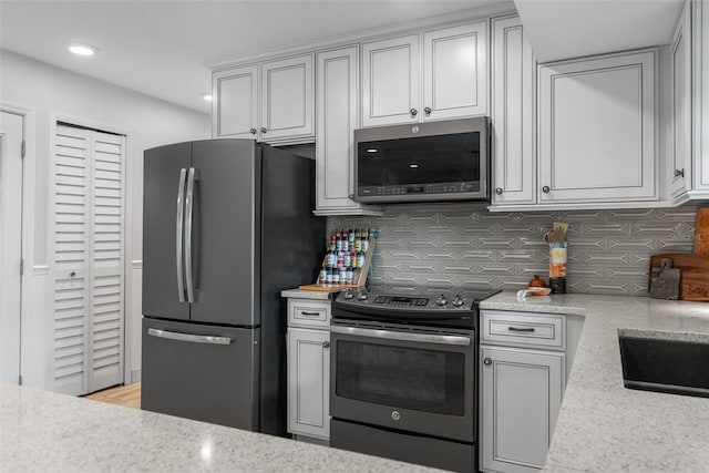 kitchen with light stone counters, decorative backsplash, and appliances with stainless steel finishes