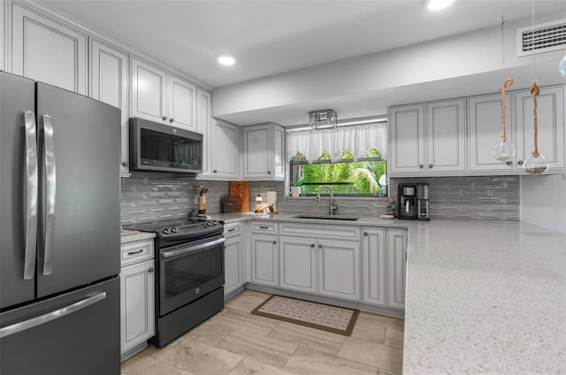 kitchen with sink, tasteful backsplash, light stone counters, gray cabinets, and stainless steel appliances