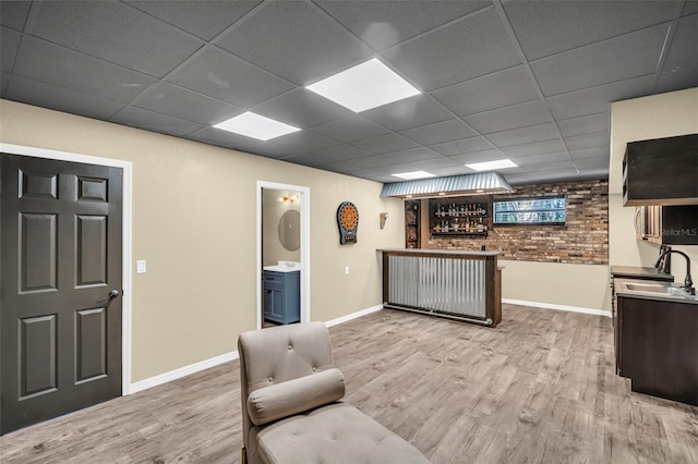 living room with brick wall, a paneled ceiling, indoor wet bar, and light hardwood / wood-style floors