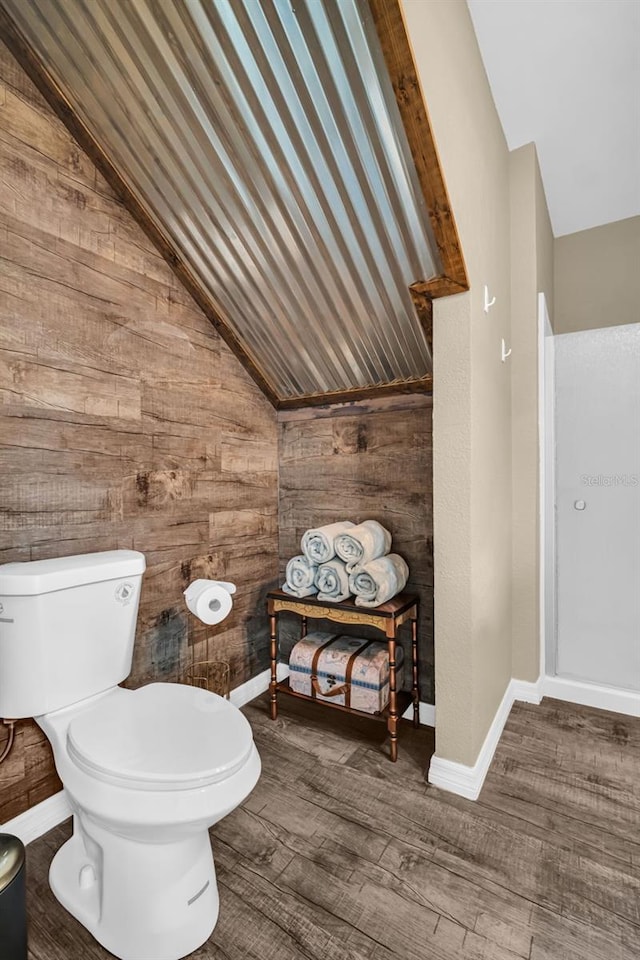 bathroom featuring wood-type flooring, vaulted ceiling, wood walls, and toilet