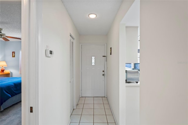 doorway with light tile patterned floors, a textured ceiling, and ceiling fan