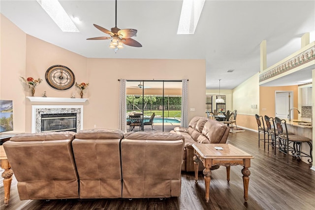 living room featuring ceiling fan, lofted ceiling with skylight, dark wood-type flooring, and a high end fireplace