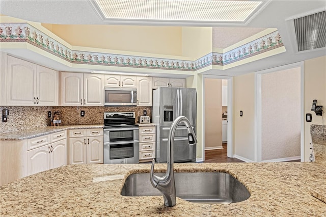 kitchen with decorative backsplash, light stone counters, sink, and appliances with stainless steel finishes