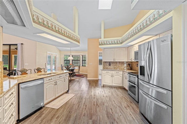 kitchen featuring appliances with stainless steel finishes, tasteful backsplash, light stone counters, sink, and light hardwood / wood-style floors