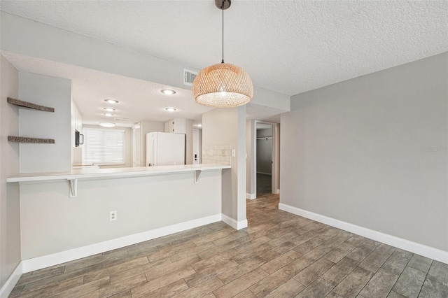 kitchen featuring decorative light fixtures, white refrigerator, a kitchen bar, and kitchen peninsula