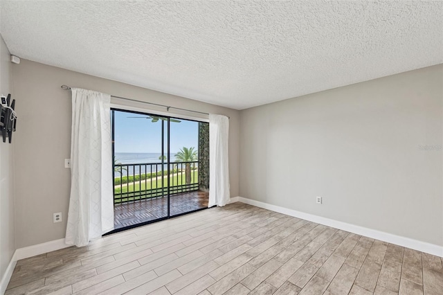 empty room with a water view, light wood-type flooring, and a textured ceiling