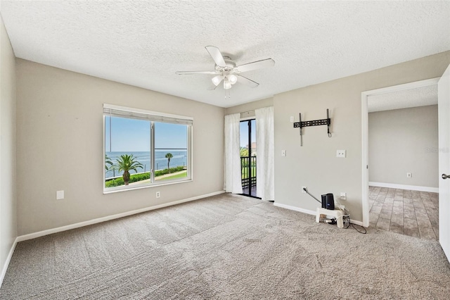 spare room with light carpet, a water view, a textured ceiling, and ceiling fan