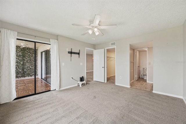 unfurnished bedroom featuring ceiling fan, a spacious closet, a textured ceiling, light colored carpet, and a closet