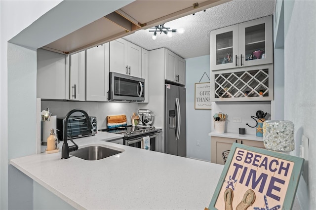 kitchen featuring white cabinetry, sink, kitchen peninsula, a textured ceiling, and appliances with stainless steel finishes