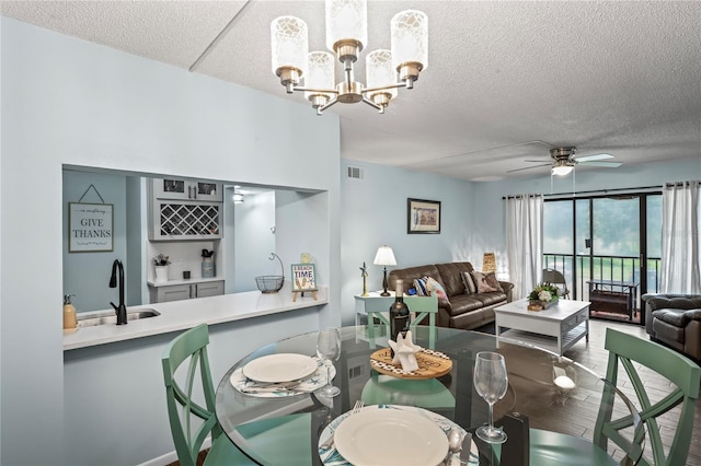 dining area featuring a textured ceiling, ceiling fan with notable chandelier, sink, and hardwood / wood-style floors