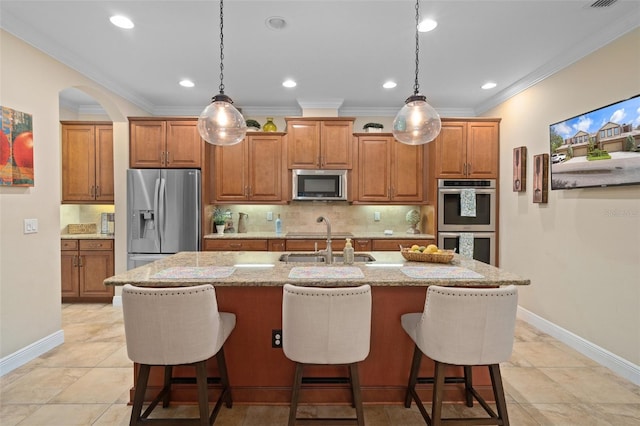 kitchen featuring light stone counters, ornamental molding, an island with sink, and appliances with stainless steel finishes