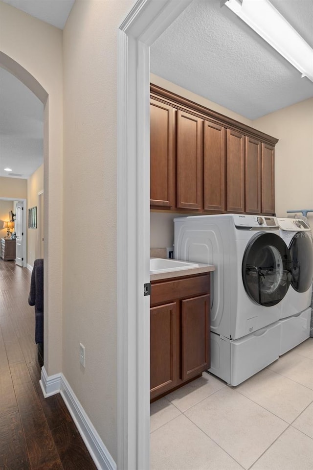 laundry area with cabinets, light hardwood / wood-style floors, washing machine and dryer, and sink