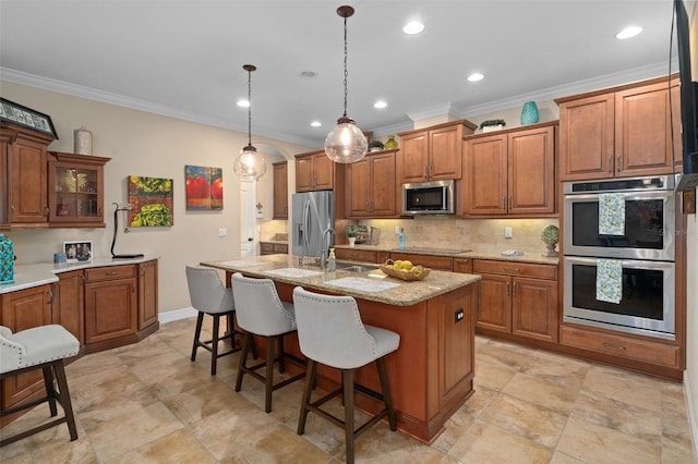 kitchen with light stone countertops, stainless steel appliances, tasteful backsplash, decorative light fixtures, and a kitchen island with sink