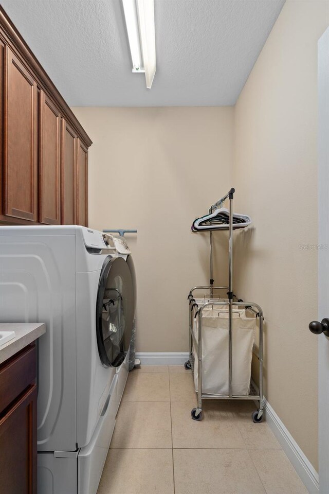 washroom with cabinets, light tile patterned floors, a textured ceiling, and washing machine and clothes dryer