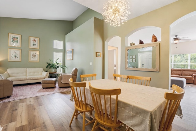 dining area featuring ceiling fan with notable chandelier, light hardwood / wood-style floors, and vaulted ceiling