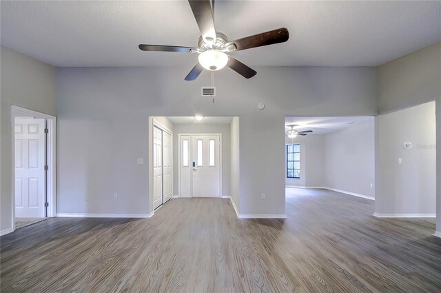 unfurnished living room featuring ceiling fan, a towering ceiling, and hardwood / wood-style flooring