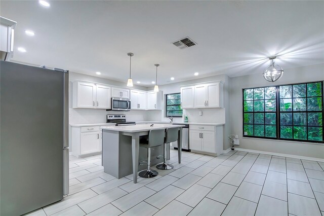 kitchen with an inviting chandelier, white cabinets, hanging light fixtures, appliances with stainless steel finishes, and a kitchen bar