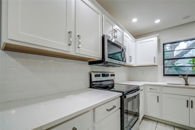 kitchen with sink, light tile patterned floors, backsplash, white cabinets, and appliances with stainless steel finishes