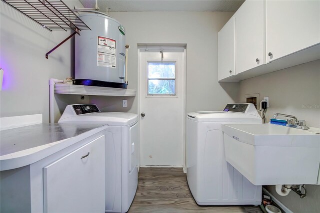 laundry room with cabinets, electric water heater, sink, light hardwood / wood-style flooring, and washing machine and dryer