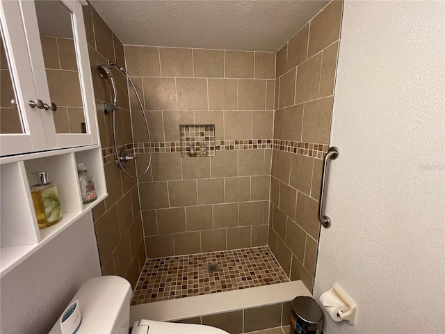 bathroom featuring a textured ceiling, toilet, and tiled shower