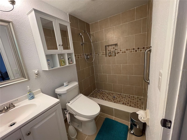 bathroom with a textured ceiling, toilet, vanity, and tiled shower