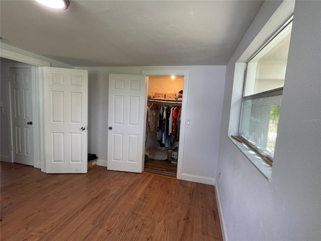 unfurnished bedroom featuring a spacious closet, wood-type flooring, and a closet