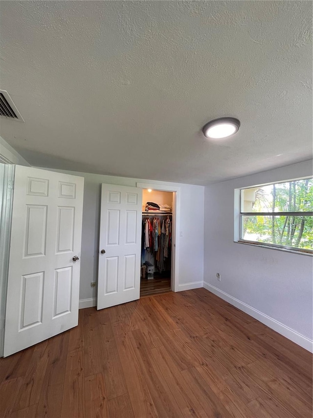 unfurnished bedroom with a spacious closet, hardwood / wood-style floors, a closet, and a textured ceiling