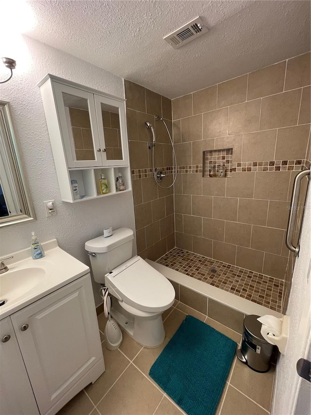 bathroom with toilet, tile patterned flooring, a textured ceiling, and a tile shower