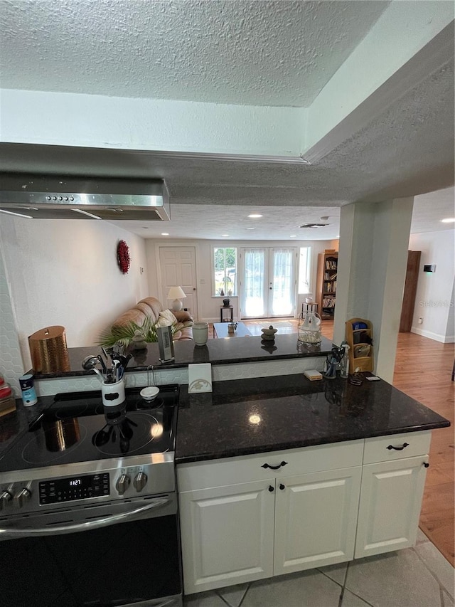 kitchen with light tile patterned floors, stainless steel electric range oven, dark stone countertops, a textured ceiling, and white cabinets