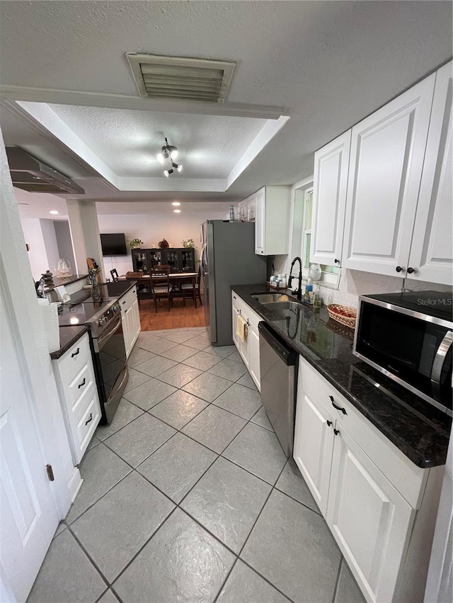 kitchen featuring a raised ceiling, sink, light tile patterned floors, stainless steel appliances, and white cabinets